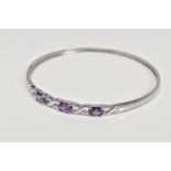 A CUBIC ZIRCONIA BANGLE, designed as three oval purple cubic zirconias interspaced by open cross