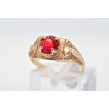 A RING, set with a circular cut red paste within a four claw setting to the textured surround and