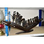 A NATIVE ART HARDWOOD CARVING OF FOURTEEN ROWERS IN A LONG BOAT standing on a wooden plinth, the