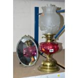 A BRASS TWIN BURNER OIL LAMP, having cranberry glass reservoir and satin finish milk glass shade