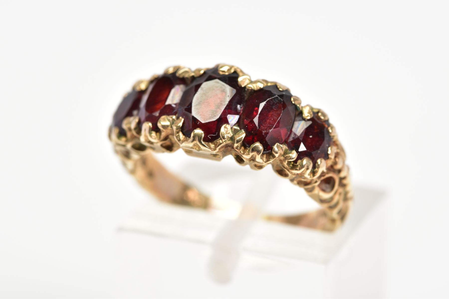 A 9CT GOLD RED GLASS RING, designed as five graduated oval cut red pastes within claw settings to