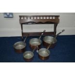 A SET OF FIVE COPPER GRADUATING PANS, with iron hooped handles and an oak hanging shelf
