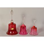 THREE VICTORIAN GLASS BELLS, with cranberry tinted bowls and turned handles, of various heights,