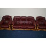 A RED LEATHER AND GOLDEN OAK THREE PIECE LOUNGE SUITE comprising of a three seater settee and a pair