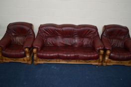 A RED LEATHER AND GOLDEN OAK THREE PIECE LOUNGE SUITE comprising of a three seater settee and a pair