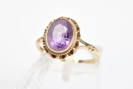 A 9CT GOLD AMETHYST RING, the oval amethyst within a collet setting with rope twist and undulating