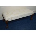 A REPRODUCTION WALNUT FOOTSTOOL with four ball and claw feet and cream upholstery, length 88cm x