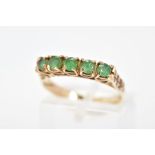 A 9CT GOLD EMERALD RING, set with a row of five circular cut emeralds to the engraved shoulders,