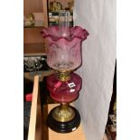 A LATE VICTORIAN CRANBERRY GLASS AND BRASS OIL LAMP, the wavy rimmed shade acid etched with floral