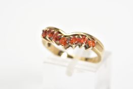 A 9CT GOLD GEM RING, the v-shape ring is claw set to the front with seven circular orange gems,