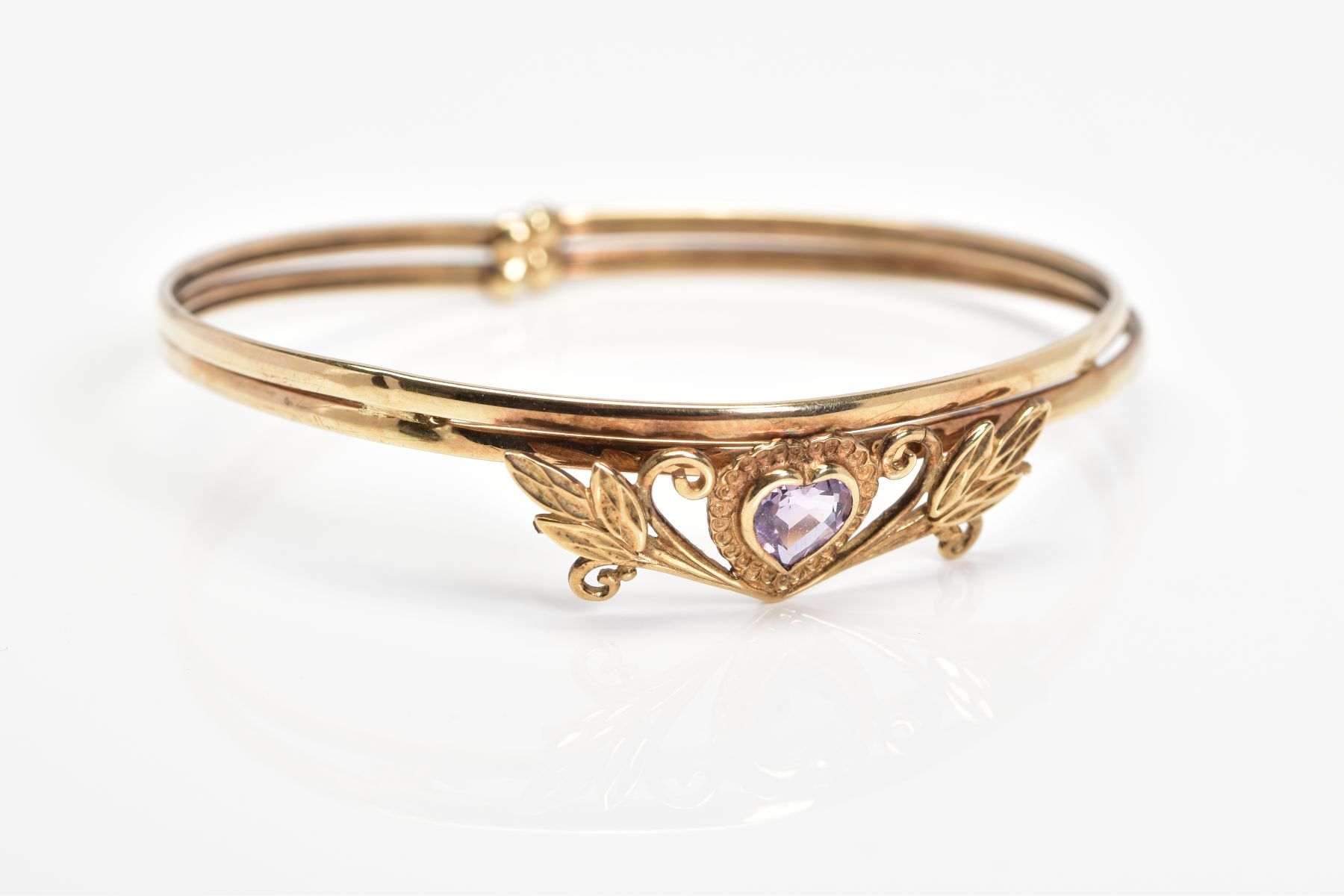 AN AMETHYST BANGLE, designed with a heart shape amethyst in a collet setting within a foliate