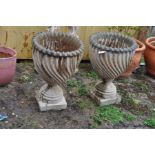 A PAIR OF COMPOSITE GARDEN URNS with a swirled fluted bowl, ring base and square foot (one piece),