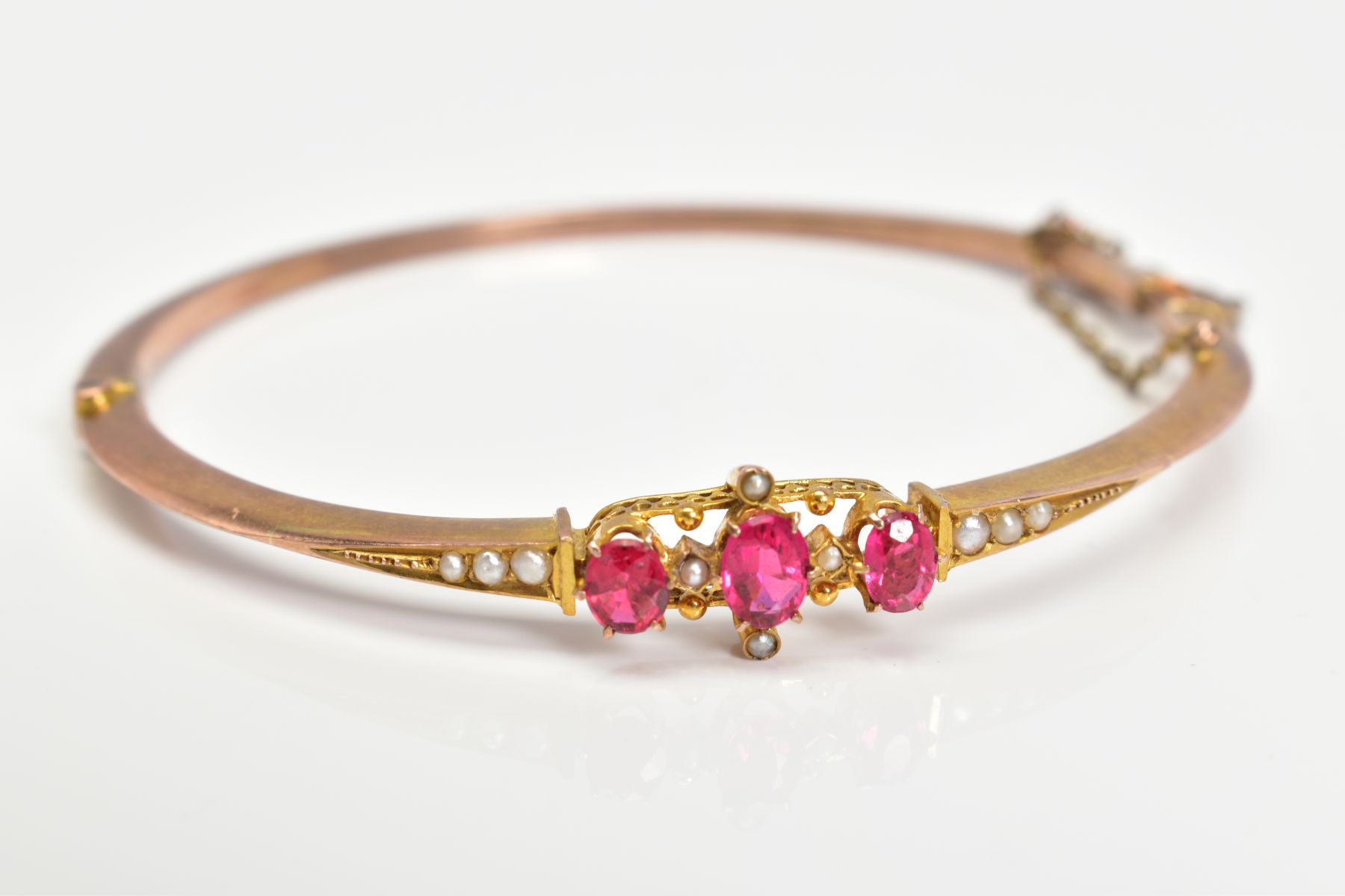 AN EARLY 20TH CENTURY GOLD SPLIT PEARL AND GARNET TOPPED DOUBLET FANCY BANGLE, measuring