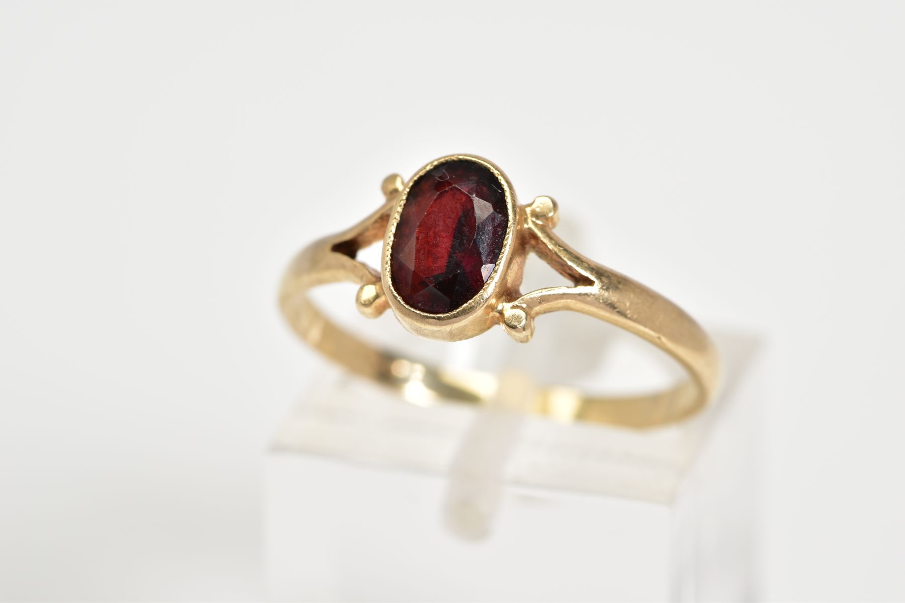 A 9CT GOLD GARNET RING, set with a central oval cut garnet to the bifurcated shoulders and plain