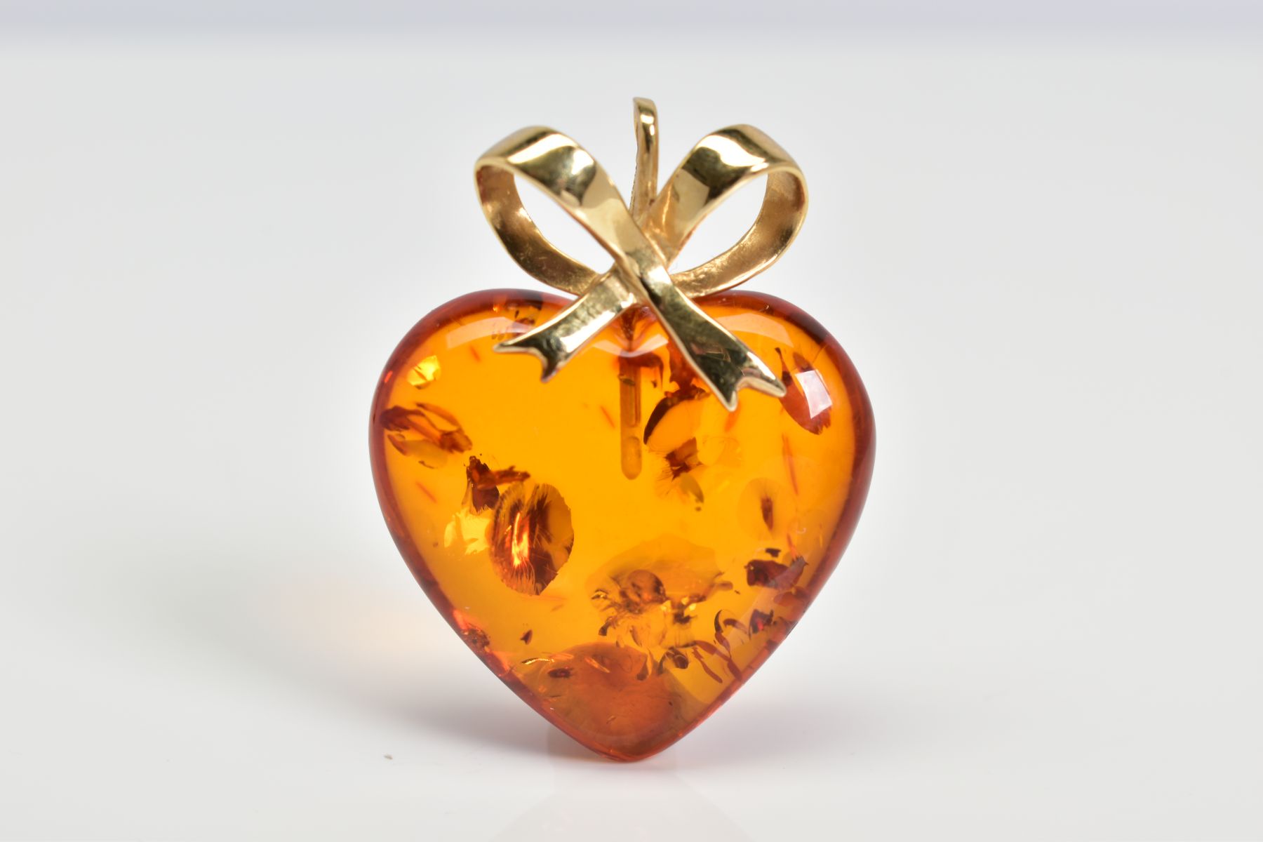 A MODERN 14CT GOLD AMBER HEART PENDANT, measuring approximately 23mm in diameter, fancy bow