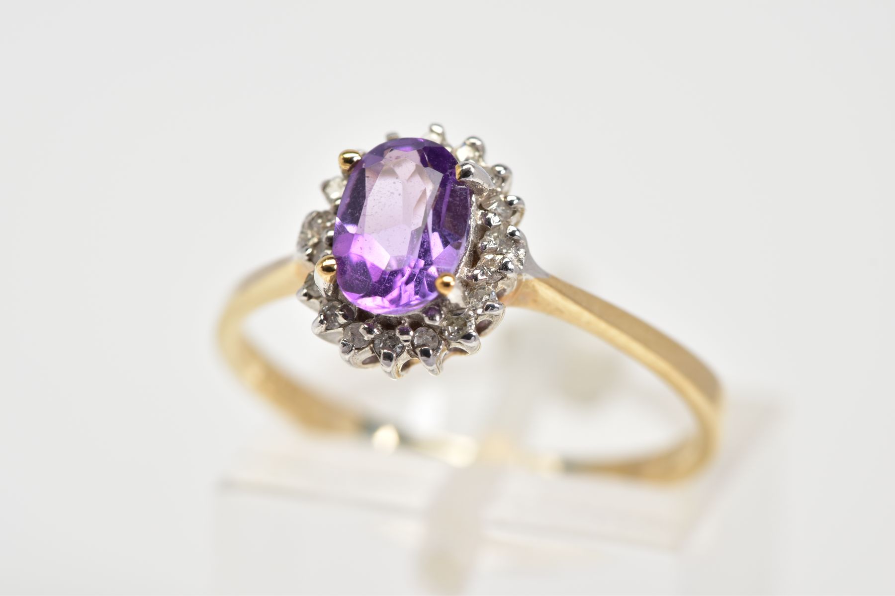 A 9CT GOLD CLUSTER RING, designed with a central oval cut amethyst and single cut diamond