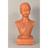 A TERRACOTTA GLAZED CERAMIC BUST OF A YOUNG BOY, on a square plinth base, chipped front corner,
