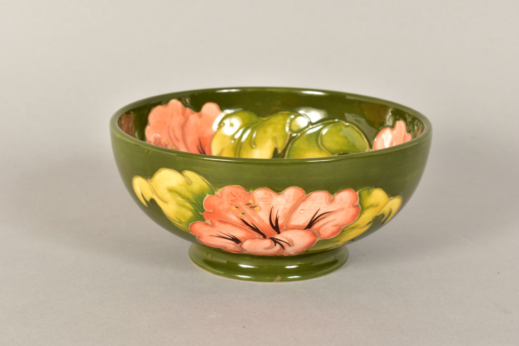 A MOORCROFT POTTERY FOOTED BOWL, 'Hibiscus' pattern on green ground, impressed backstamp and painted