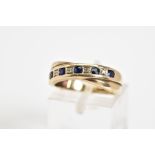 A 9CT GOLD CROSS OVER RING, set with a diagonal row of circular cut sapphire interspaced with