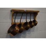 A SET OF FIVE GRADUATING COPPER PANS, with iron hooped handles on a beech hanging rack (6)