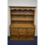 A 20TH CENTURY PINE KITCHEN DRESSER, the top with a wavy apron above two plate racks, three drawers,