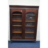 AN EDWARDIAN MAHOGANY DOUBLE DOOR BOOKCASE on turned legs with ceramic casters, width 130cm x