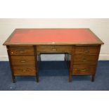 A MID 20TH CENTURY STAINED OAK KNEE HOLE DESK, with a red leather top and seven drawers with brass