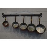 A SET OF FIVE GRADUATING COPPER PANS, with an iron hooped handles on a wrought iron hanging rack (