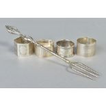 FOUR SILVER NAPKIN RINGS AND A SILVER BREAD FORK, the napkin rings of various designs to include