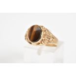 A 9CT GOLD SIGNET RING, set with an oval tigers eye panel within a collet mount to the embossed
