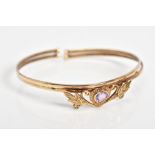 AN AMETHYST SET BANGLE, set with a central heart shaped amethyst within a floral detail panel, to