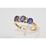 AN 18CT GOLD TANZANITE AND DIAMOND RING, designed with three oval cut tanzanite's interspaced with