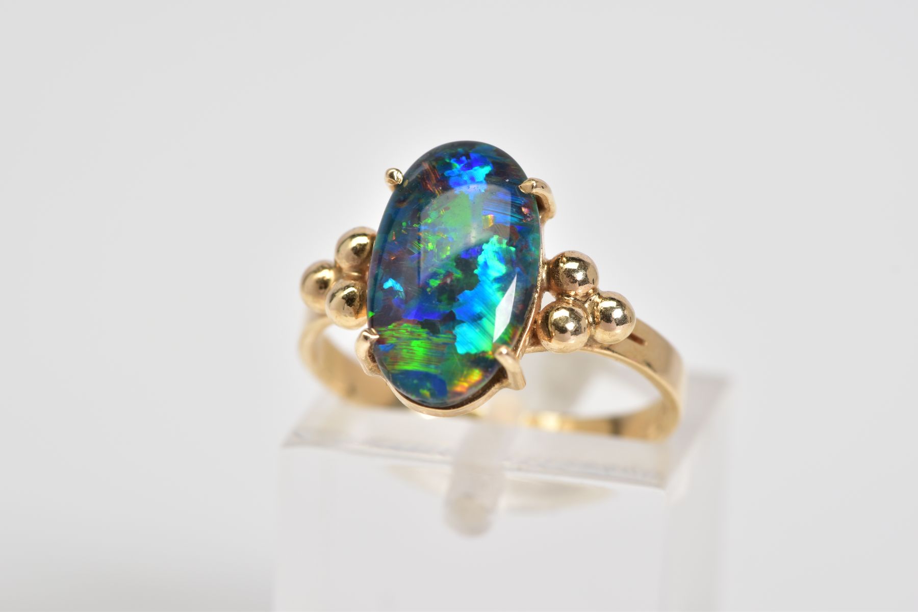 AN OPAL TRIPLET RING, the oval opal triplet set within a four claw setting, to the bead detail