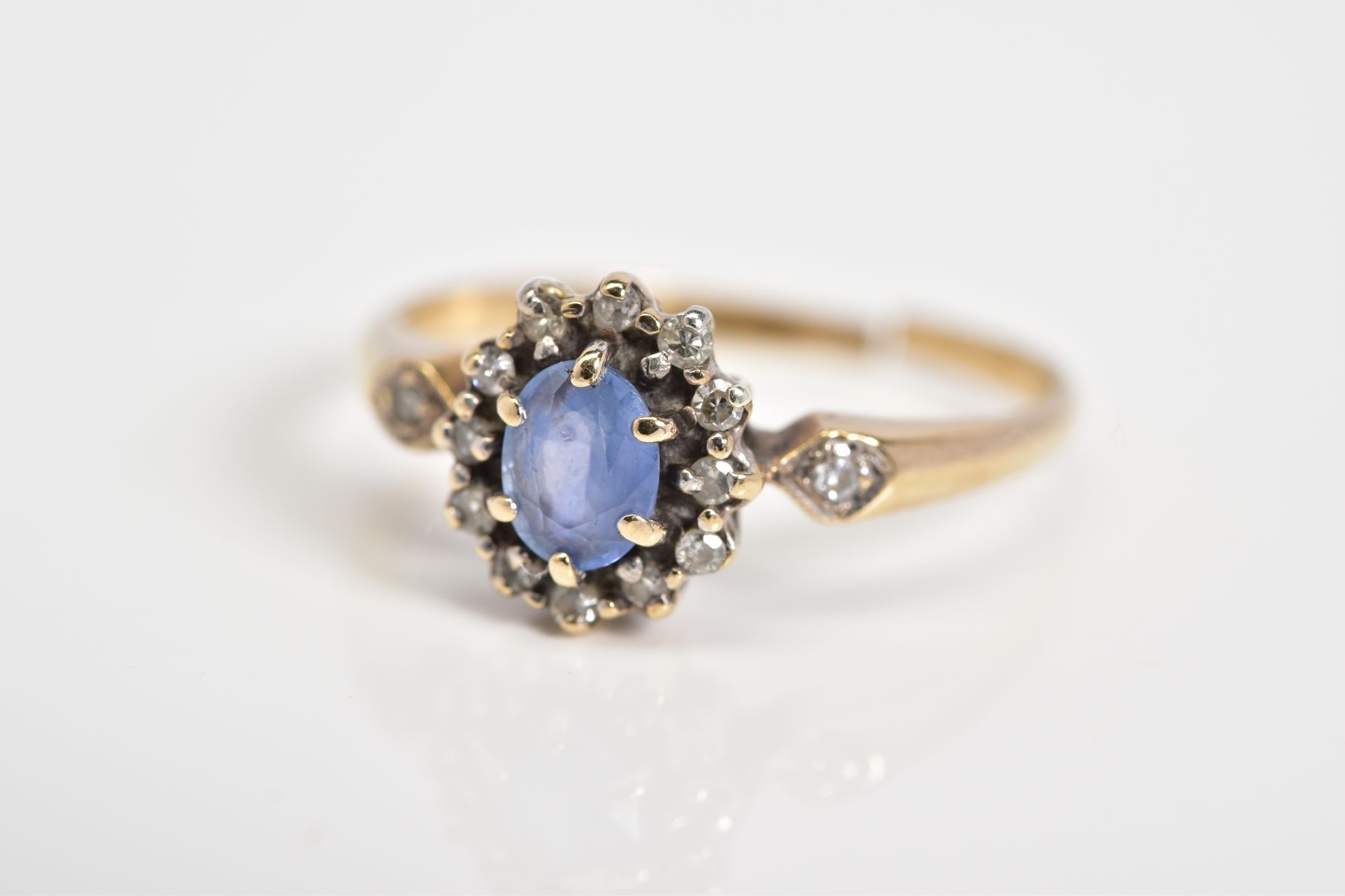 A 9CT GOLD CLUSTER RING, set with a central oval cut sapphire, single cut diamond surround to the