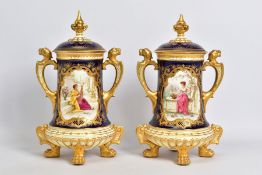 A PAIR OF EARLY 20TH CENTURY COALPORT TWIN HANDLED URNS AND COVERS WITH HAND PAINTED PANELS OF