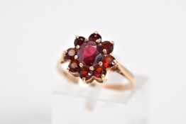 A GARNET CLUSTER RING, designed with a raised cluster set with nine circular cut garnets, to the