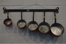 A SET OF FIVE GRADUATING COPPER PANS, with an iron hooped handles on a wrought iron hanging rack