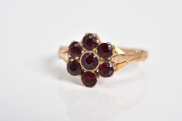 A GARNET SET CLUSTER RING, the yellow metal ring designed as a cluster set with seven circular cut