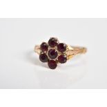 A GARNET SET CLUSTER RING, the yellow metal ring designed as a cluster set with seven circular cut