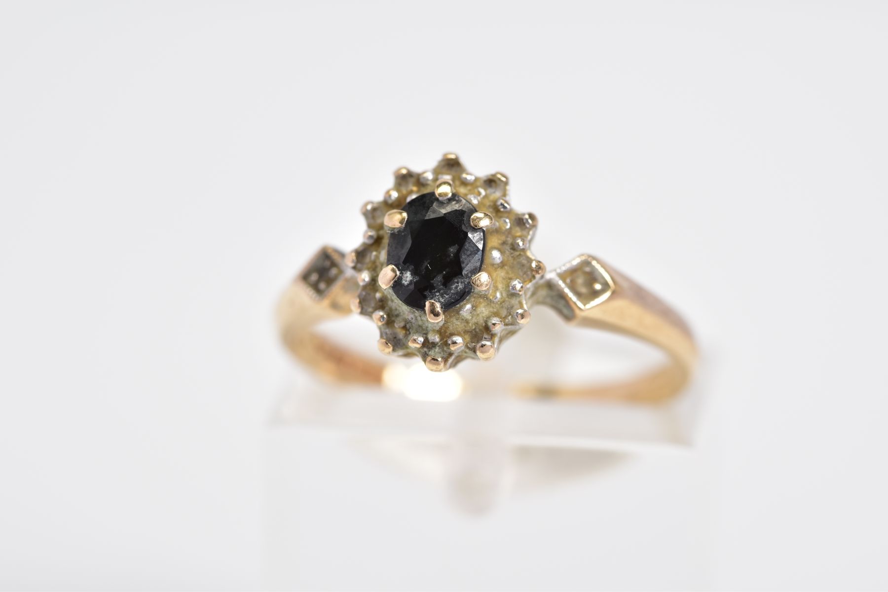 A 9CT GOLD SAPPHIRE AND DIAMOND CLUSTER RING, set with a central oval cut sapphire within a single