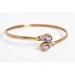 A 9CT GOLD CROSSOVER BANGLE, the open bangle set with two oval cut amethyst and single cut diamond