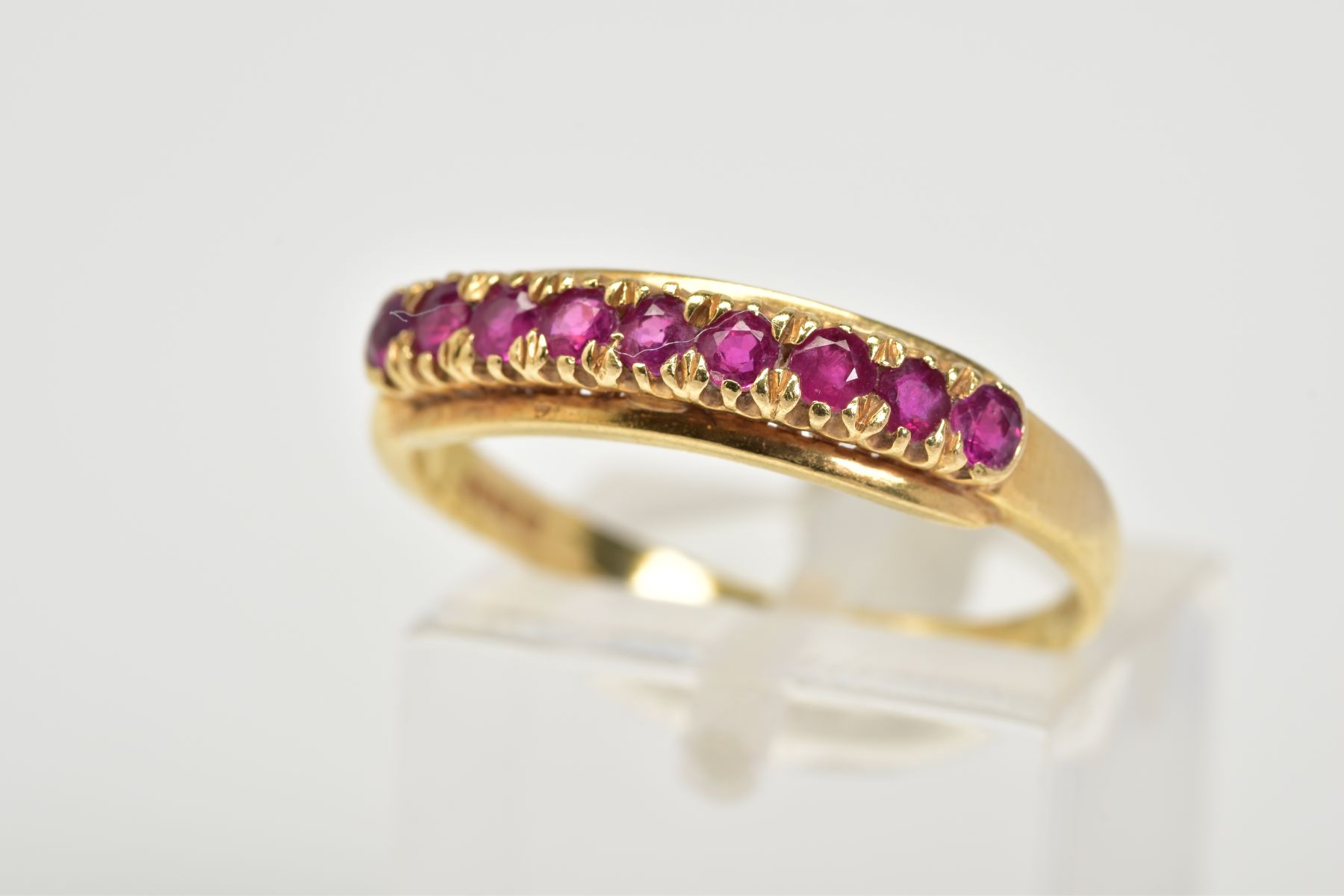 AN 18CT GOLD RUBY RING, of half hoop design set with nine circular cut claw set rubies, to a plain