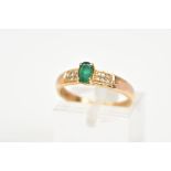 AN EMERALD AND DIAMOND RING, the yellow metal ring designed with a central oval cut emerald