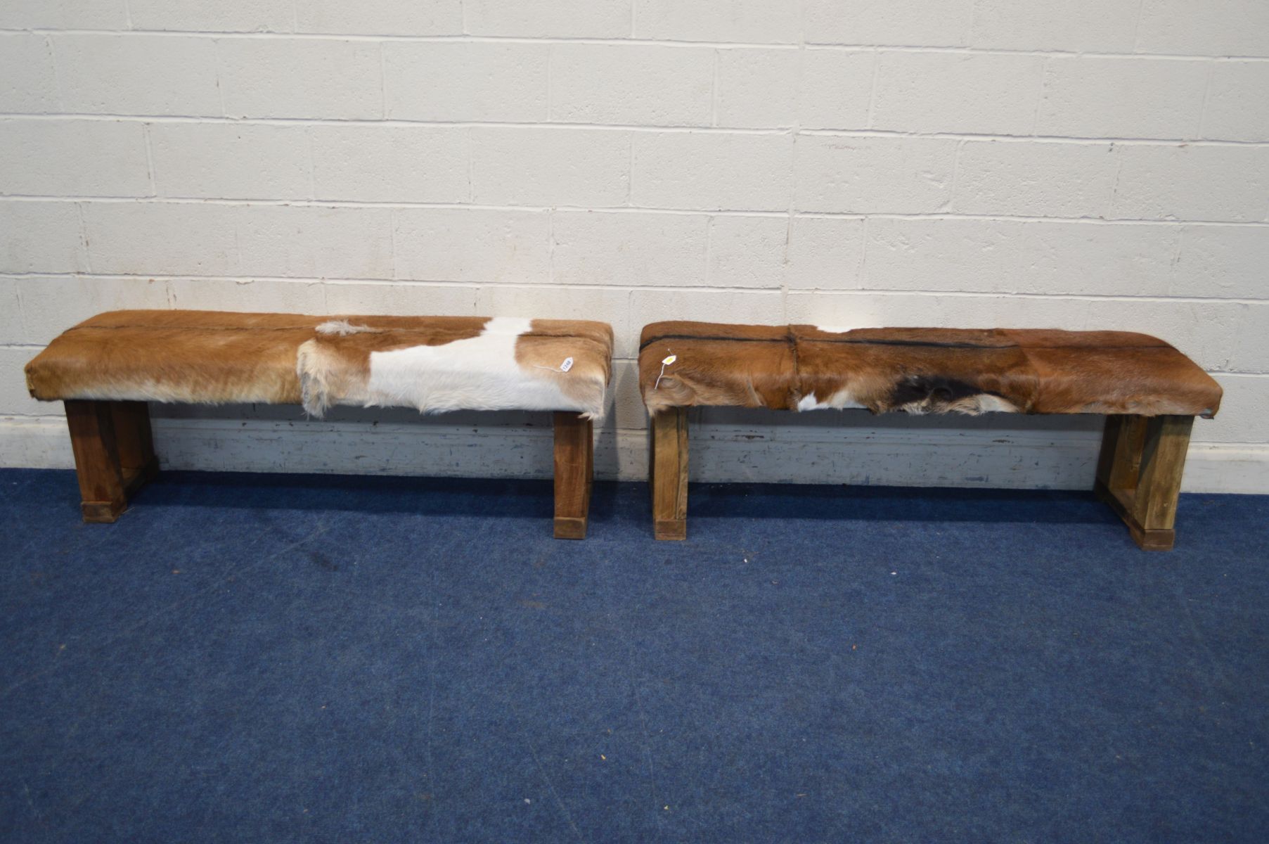 A PAIR OF RUSTIC RECTANGULAR STOOLS with animal hide seat covers, width 152cm x depth 44cm x