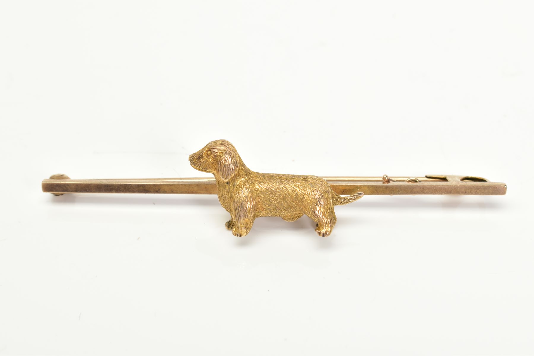 A 9CT GOLD BAR BROOCH, set with a textured dog, to the plain polished bar with a 9ct hallmark,