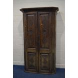 A DISTRESSED EARLY 20TH CENTURY CARVED OAK TWO DOOR WARDROBE, with overhanging cornice, canted front