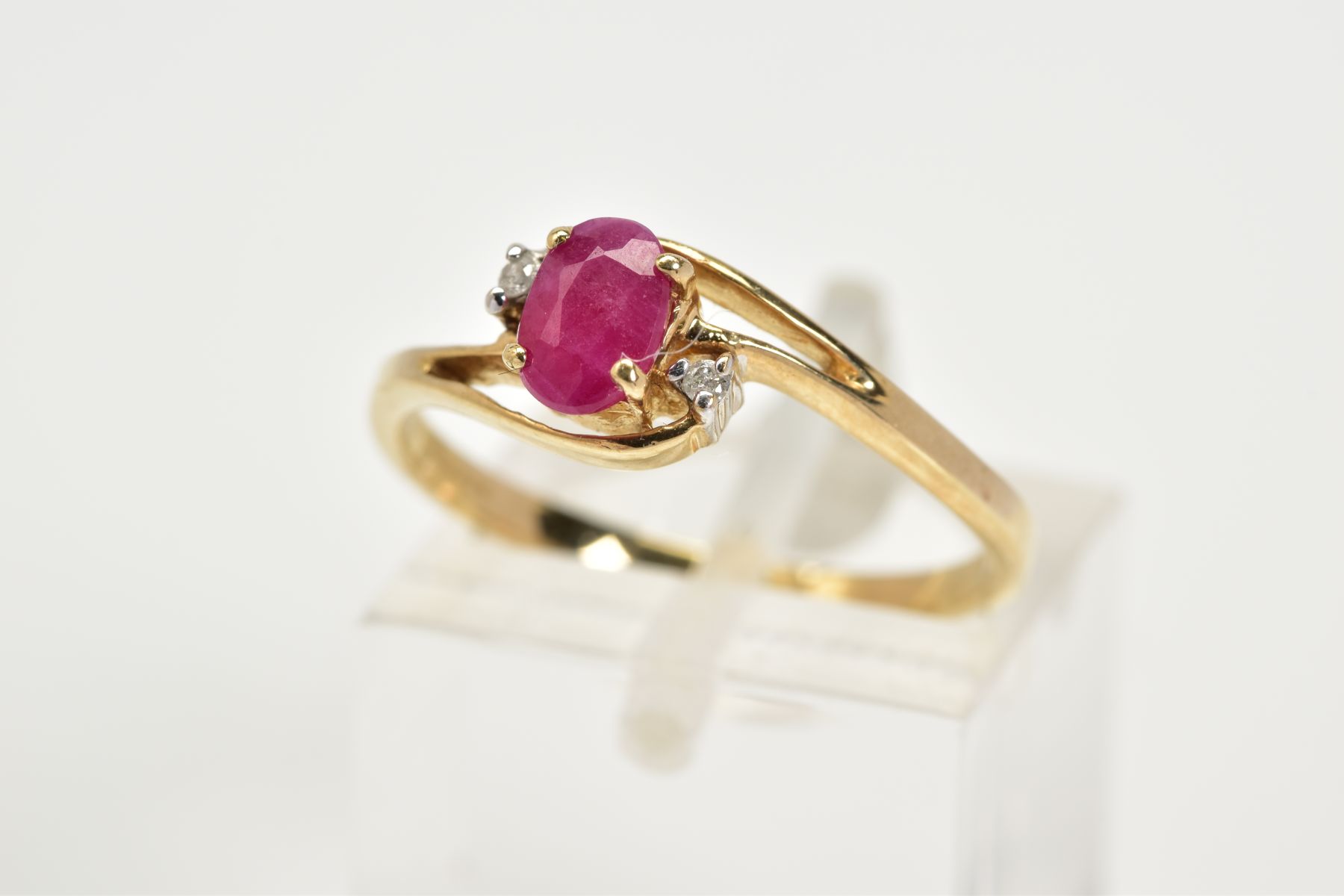 A 9CT GOLD RUBY AND DIAMOND RING, the openwork crossover design, with a central claw set oval cut