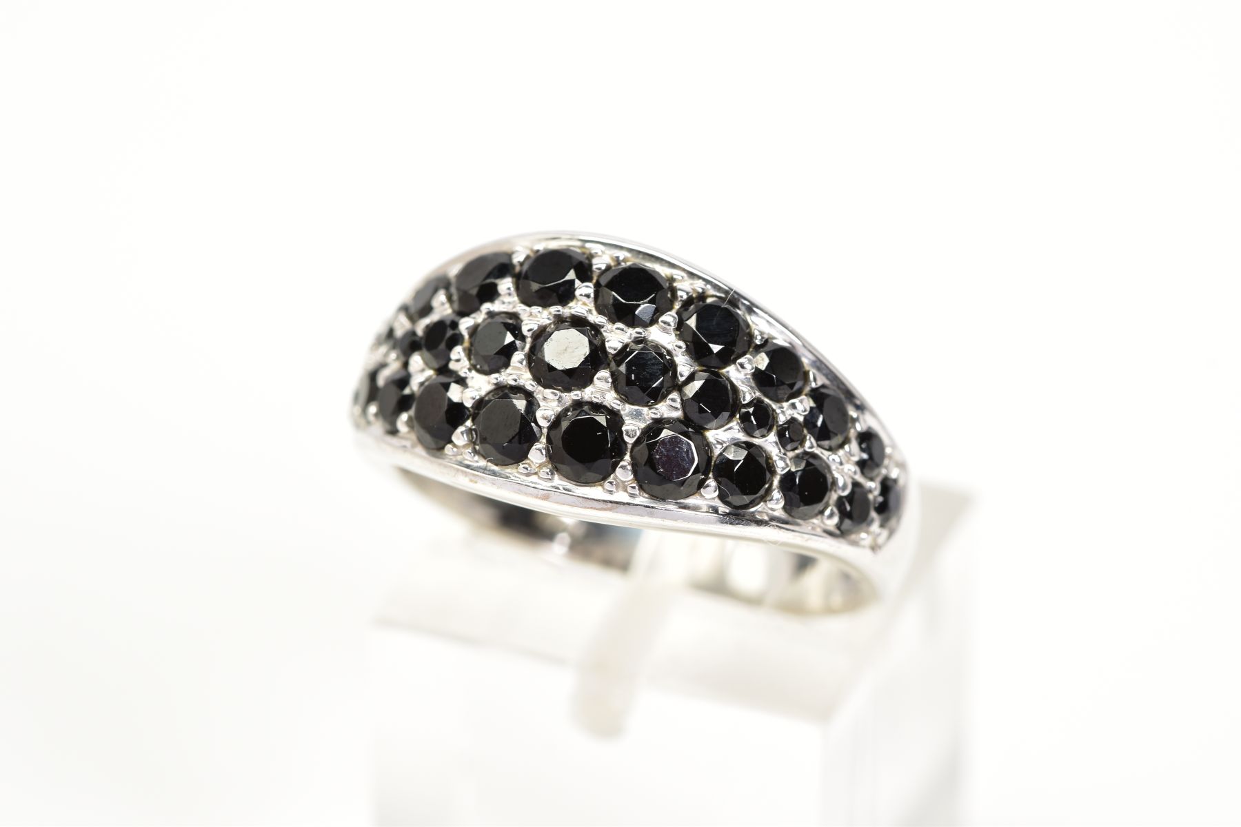 A GEM SET RING, the white metal ring designed with an oval panel set with circular cut black