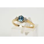 A 9CT GOLD THREE STONE RING, designed with a claw set oval blue stone assessed as topaz, flanked