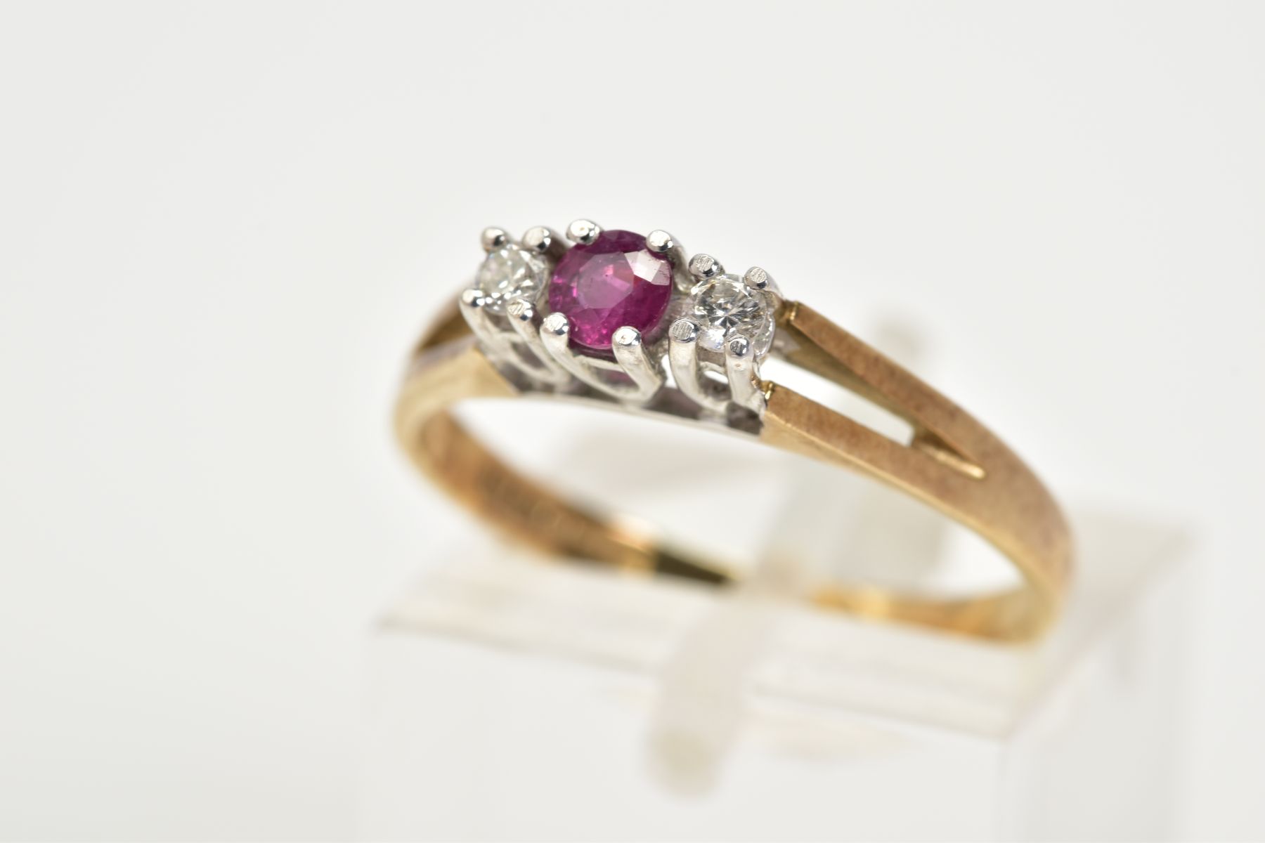 A 9CT GOLD THREE STONE RING, designed with a central claw set circular cut ruby flanked by round